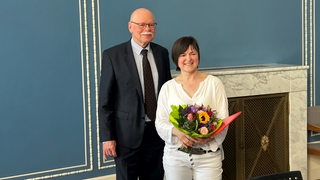 Innensenator Ulrich Mäurer und Ute Kraft-Uhlhorn posieren für die Fotografen, sie trägt einen Blumenstrauß