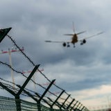 Ein Flugzeug befindet sich im Landeanflug auf den Rheinmain-Airport, im Vordergrund ein Zaun mit Stacheldraht.