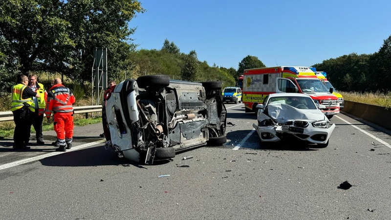 Nach einem Unfall auf einer Autobahn liegt ein stark beschädigtes Auto auf der Seite. 