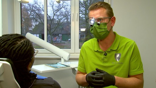 Zahnarzt mit Lupen über Brille und Licht erklärt einer Patientin die Behandlung