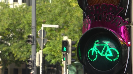 Mehrere auf grün geschaltete Fußgängerampeln an einer Straßenkreuzung mit einem Happy Birthday Schild