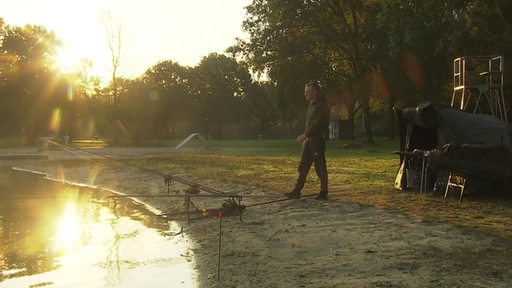 Der Angler Philipp Logemann bewegt sich aus einem Zelt auf das Seeufer und einigen Angeln zu