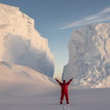 Ein Mann reckt die Arme in die Höhe während er vor riesigen Schneebergen steht.