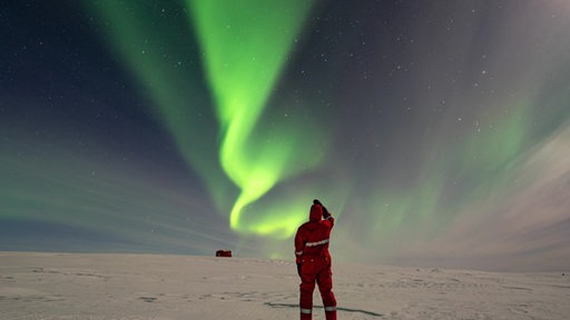 Ein Mann beobachtet Polarlichter über einer Schneelandschaft in der Antarktis.