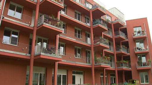 Es ist ein rotes Wohngebäude mit mehreren Balkonen zu sehen.