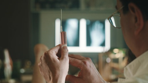 Ein Arzt hält eine Spritze mit einer leicht rötlichen Flüssigkeit in die Höhe.