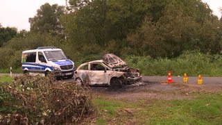 Ein abgebranntes Auto steht an einem Weg.