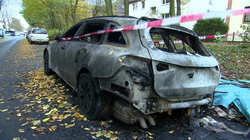 Ein ausgebranntes Auto steht am Straßenrand.