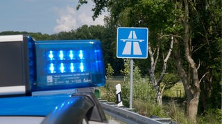 Ein Polizeiauto mit Blaulicht steht vor einem Autobahnschild.