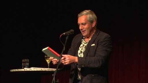 Der Deutsch-Russe Wladimir Kaminer hält sein Buch in den Händen und ließt daraus auf einer Bühne in Bremerhaven.