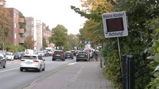 Mehrere Autos fahren über eine Straße an einem Geschwindigkeitsanzeiger vorbei