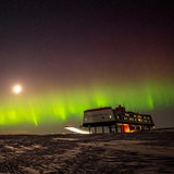 Polarlichter leuchten hinter einer Forschungsstation in der Antarktis.