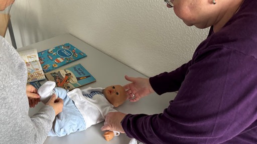 Eine Frau zeigt jungen Frauen an einer Puppe, wie ein Baby gewickelt wird