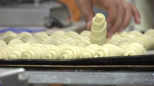 Eine Hand platziert Croissants auf einem Blech