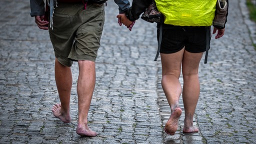 Ein Paar geht barfuß bei Regenwetter über Kopfsteinpflaster.