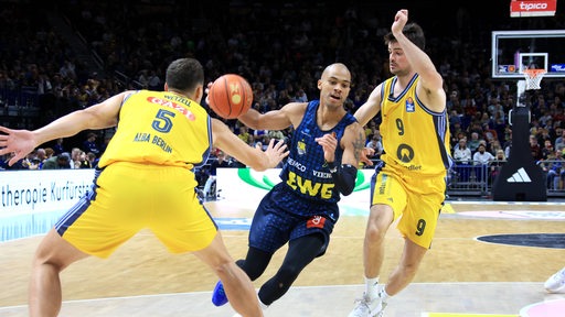 Oldenburgs Basketballer Geno Crandall dribbelt mit dem Ball, die Berliner Gegenspieler versuchen zu blocken.