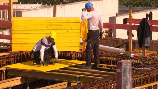 Zwei Bauarbeiter bauen auf einer Baustelle.