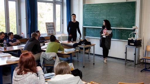 Klassenraum einer Berufsschule mit mehreren Schülern und einer Lehrerin