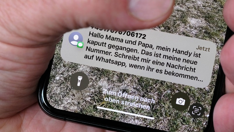 Ein Finger hält auf einen Smartphone-Display, auf dem gerade eine Betrugs-Nachricht eingegangen ist.