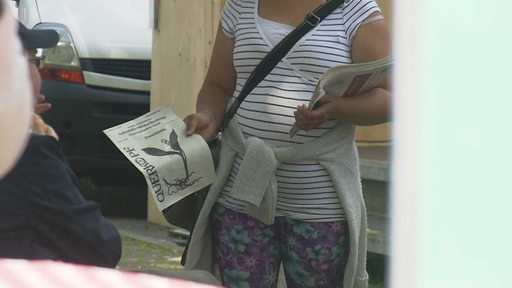 Eine Frau hält einer sitzenden Person eine Zeitung hin.