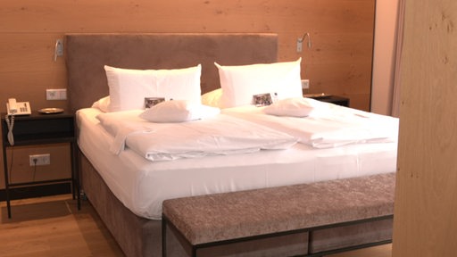 In einem Hotelzimmer ist ein großes Doppelbett zu sehen.