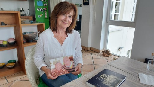 Eine Frau sitzt an einem Tisch und hält ein Foto in den Händen.