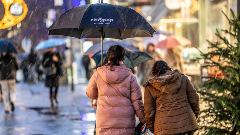 Passanten mit Regenschirmen gehen in der Innenstadt an einem Weihnachtsbaum vorbei