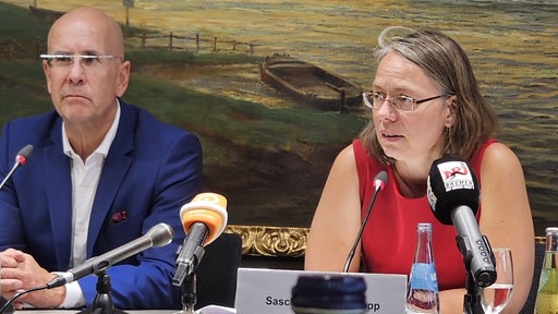 Bremens Bildungssenatorin Sascha Aulepp (SPD) sitzt während einer Pressekonferenz neben ihrem Staatsrat auf dem Podium.