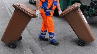 Ein Mitarbeiter der Abfallwirtschaft schiebt eine braune Tonne mit Biomüll zum Müllwagen. 