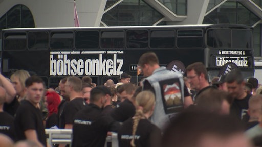 Ein schwarzer Bus der Band Böhse Onkelz auf der Bremer Bürgerweide, im Vordergrund sind Fans zu sehen.