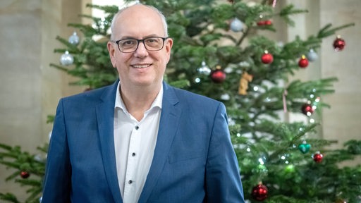 Andreas Bovenschulte steht vor einem Weihnachtsbaum im Rathaus.