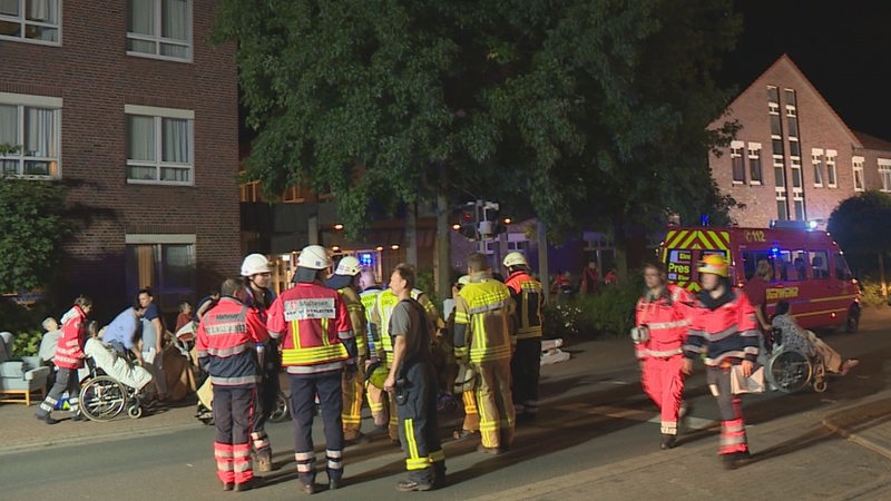 Feuerwehrkräfte und Altenheimbewohner stehen auf einer Straße.