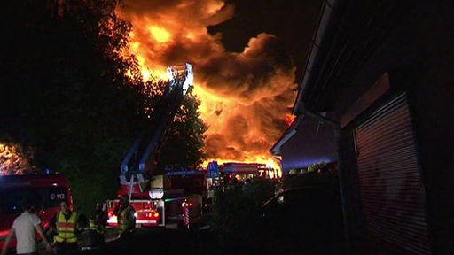 Einige Feuerwehrfahrzeuge stehen vor einem riesigen Feuerball 