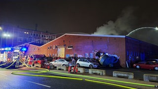 Feuerwehrkräfte löschen ein Feuer in einer Lagerhalle.