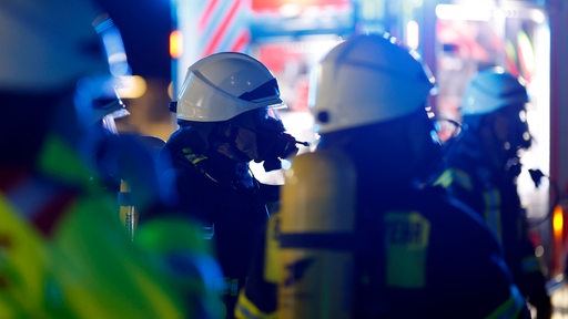 Feuerwehrleute stehen in Arbeitskleidung vor einem Feuerwehrauto.