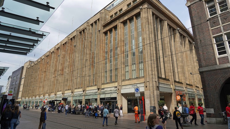 Im Zentrum des Bildes ist die Bremer Karstadt-Filiale zu sehen, vor der mehrere Passanten die Obernstraße entlanglaufen.