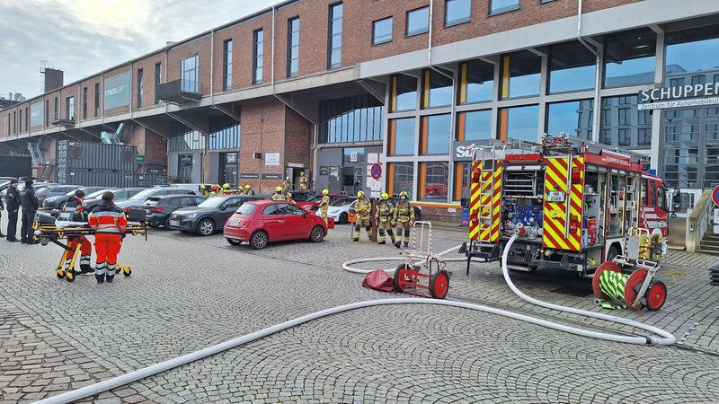 Vor einem Gebäude in der Bremer Überseestadt sind mehrere Feuerwehrleute im Einsatz.
