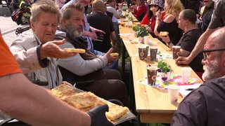 Mehrere Menschen auf Bierbänken essen Butterkuchen und trinken Kaffee.