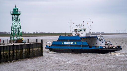 Die Weserfähre fährt an einem Leuchtturm entlang über das Wasser.