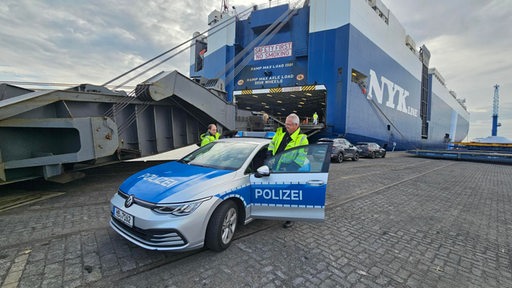 Zwei Wasserschutzpolizisten steigen vor einem im Hafen liegenden Frachter aus ihrem Auto.