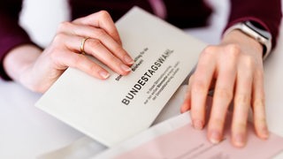 Eine Frau steckt einen Stimmzettelumschlag für die Briefwahl zur Bundestagswahl 2025 in den roten Wahlbriefumschlag.