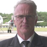 Ein Mann mit Krawatte steht vor einem Flugzeug.