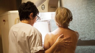 Eine älSenioren während einer Mammographie-Untersuchung, danaben eine Arzthelferin (Symbolbild)