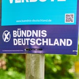 Ein Wahlplakat hängt vor grünem Hintergrund an einem Pfeiler.