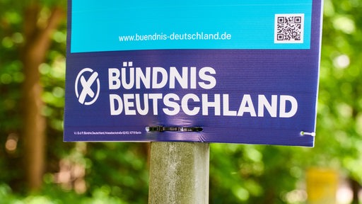 Ein Wahlplakat hängt vor grünem Hintergrund an einem Pfeiler.