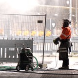 Ein Bauarbeiter steht vor einem Bauzaun und einem Schlauch