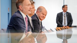 Bundeskanzler Olaf Scholz (SPD) sitzt mit Robert Habeck (Grüne) und Christian Lindner (FDP) bei einer Pressekonferenz auf dem Podium.