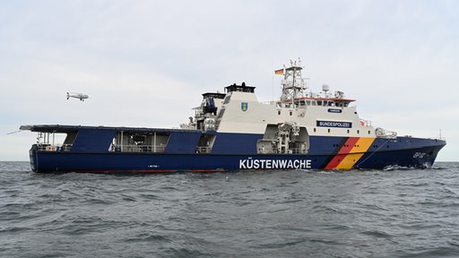 Eine Drohne landet auf einem blau-weißen Schiff mit der Aufschrift "Küstenwache".