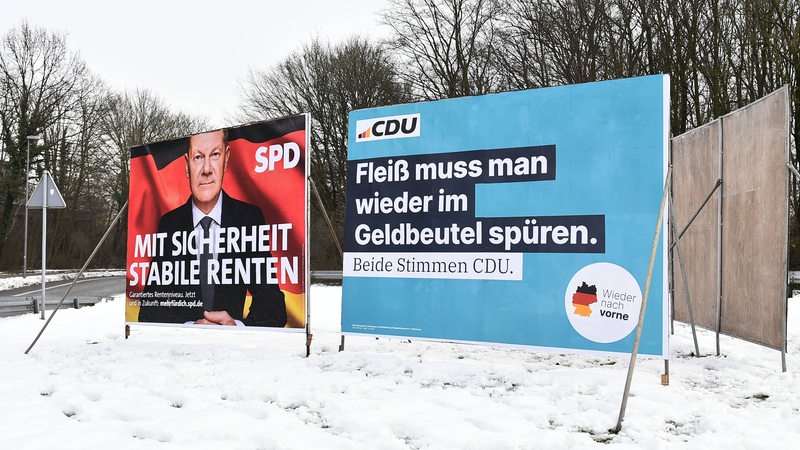 Zwei Wahlplakate stehen an einer Straße.