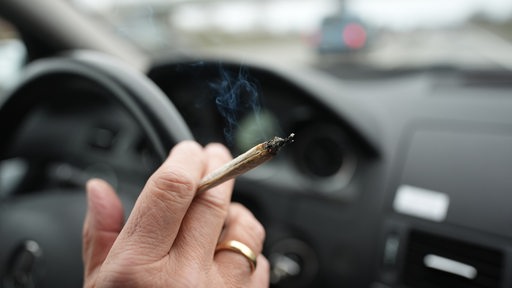 Ein Mann raucht während der Autofahrt auf einer Autobahn am Steuer einen Joint.